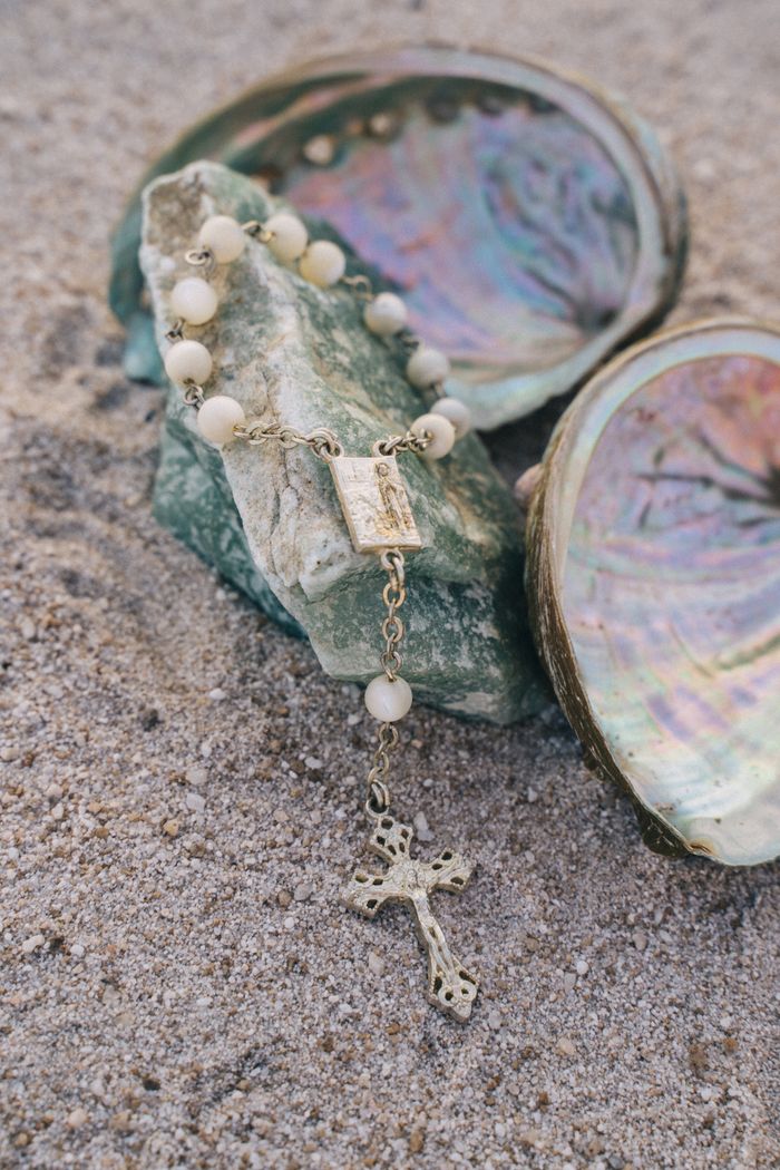 A detailed shot of a rosary placed on sand with seashells, highlighting religious symbolism.