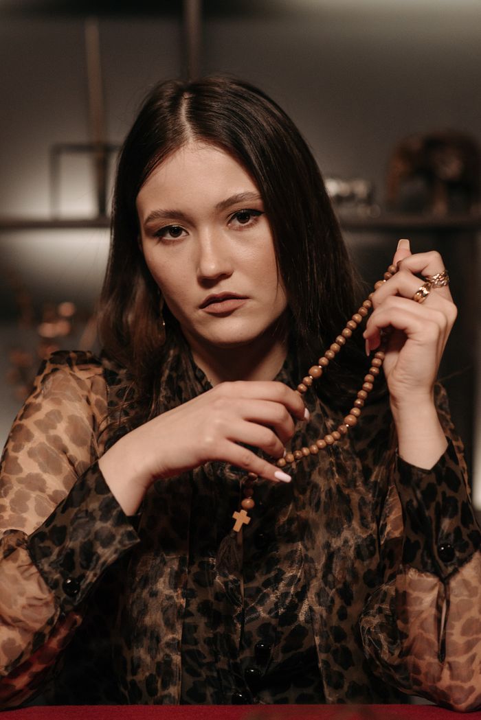 A mysterious woman with a rosary, evoking a sense of intrigue and mysticism indoors.