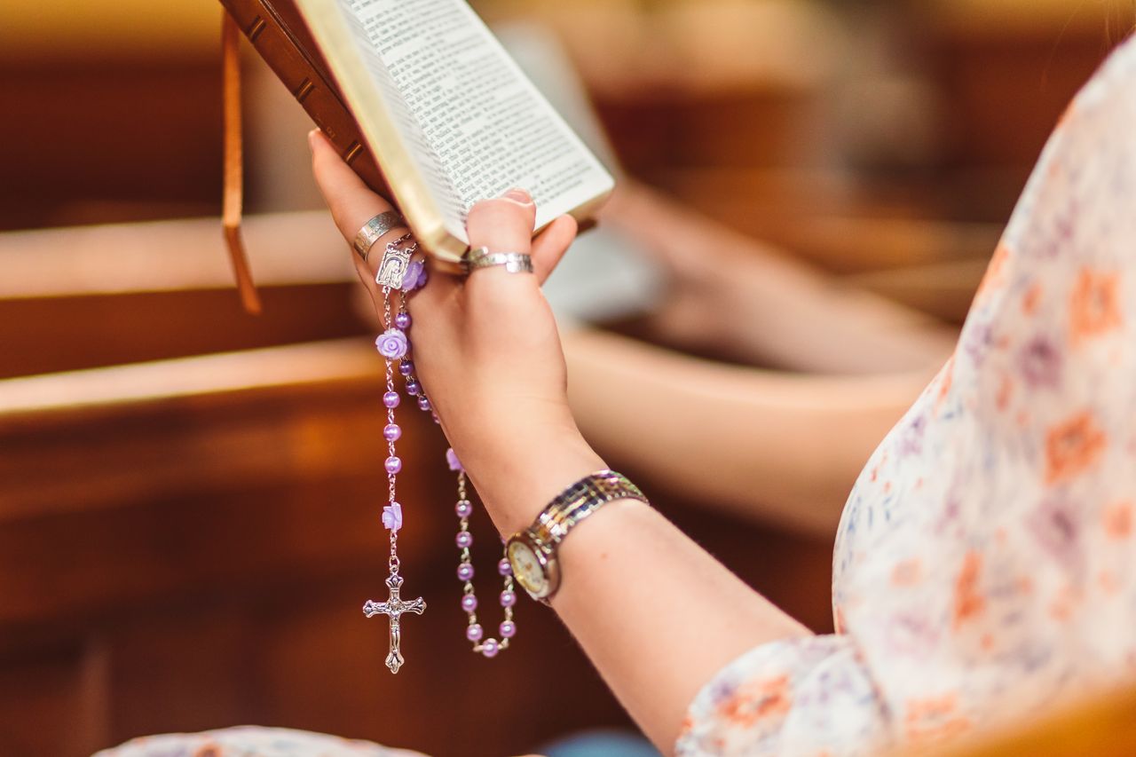 A woman reads a Bible in church while holding a rosary, showcasing faith and reflection.